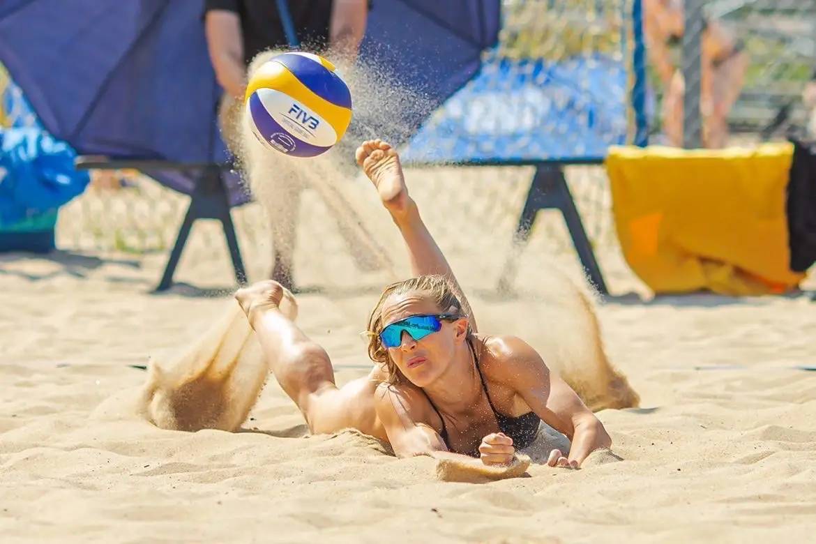 Kvinna som spelar beachvolleyboll och slänger sig i sanden